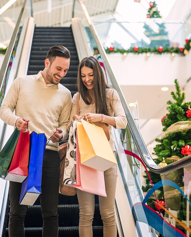 Couple going down escalator in shopping centre, Christmas time