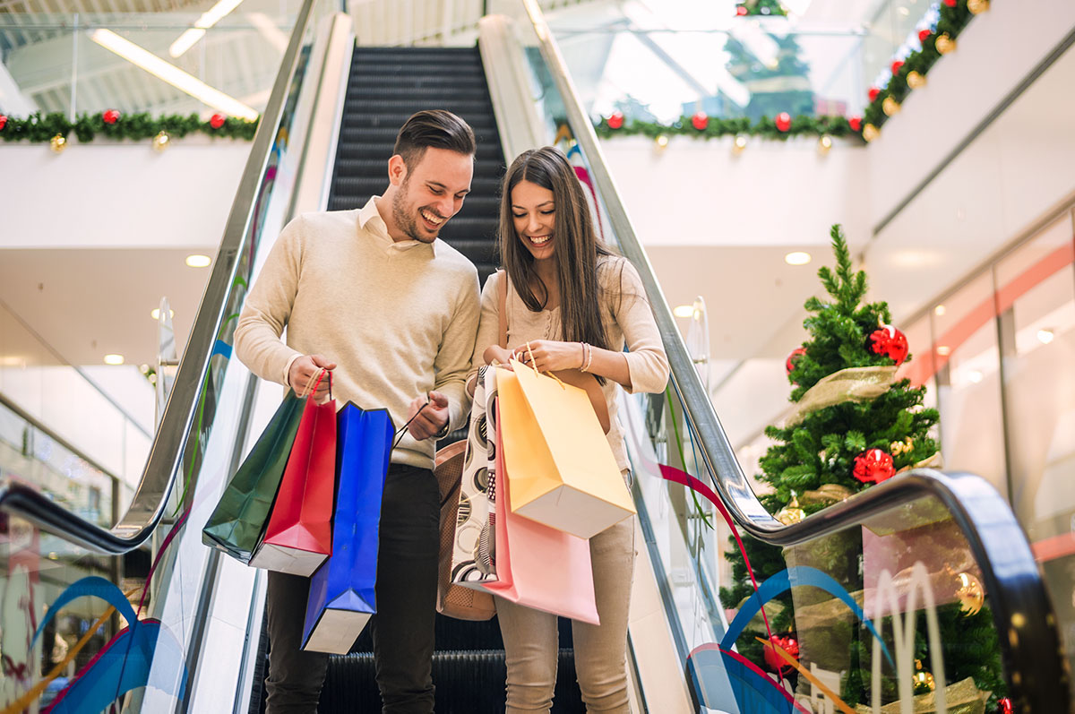 Couple going down escalator in shopping centre, Christmas time